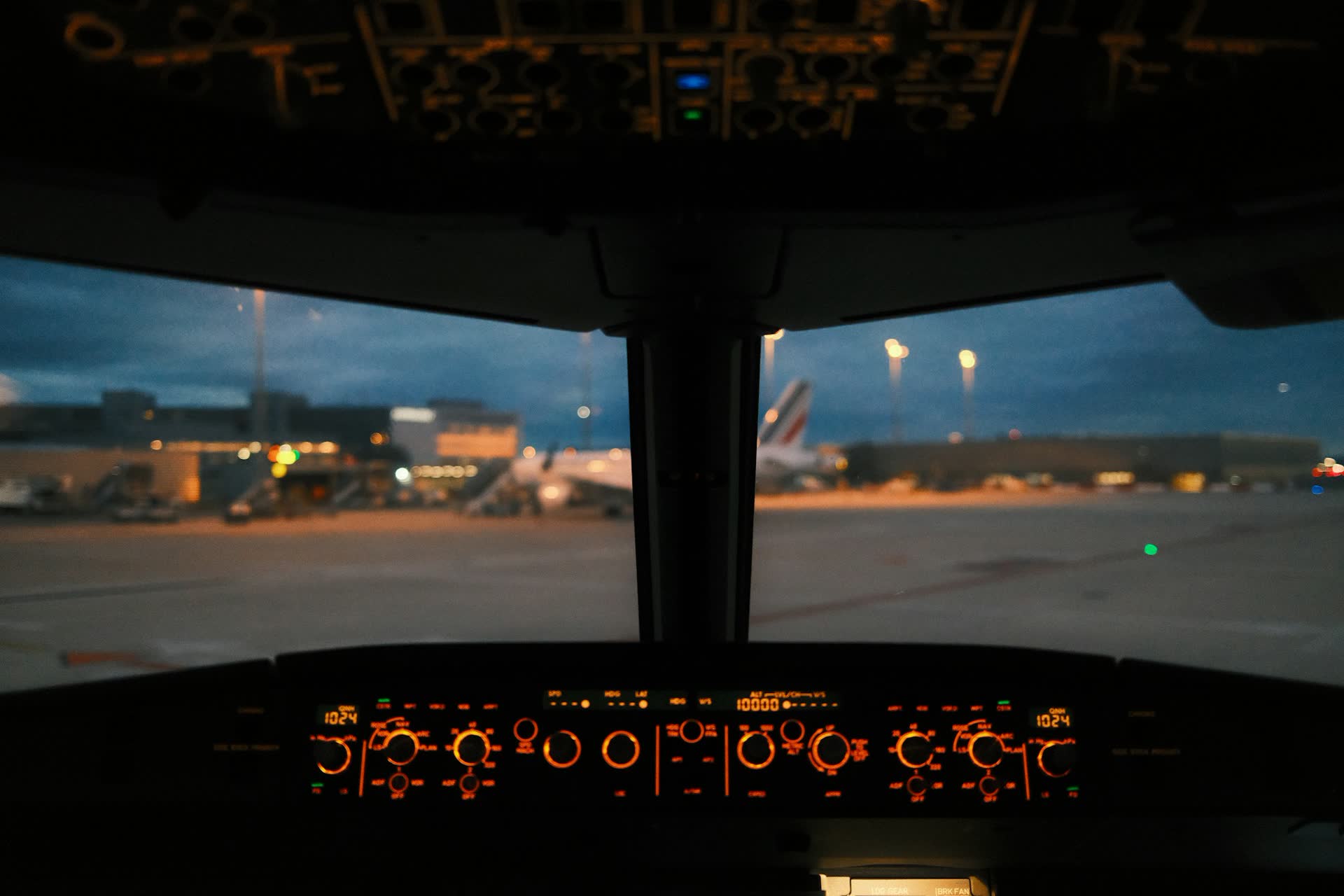 Blick aus dem Cockpit auf das beleuchtete Vorfeld in der Dämmerung