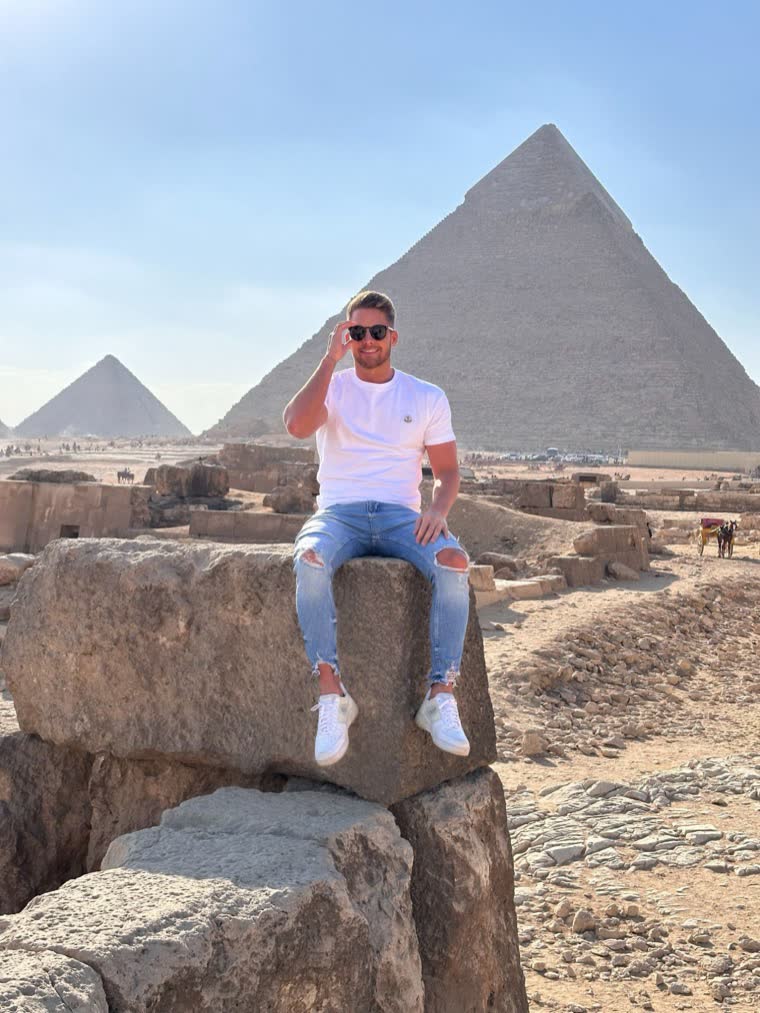 Ben sitzt auf einem Steinblock vor den Pyramiden von Gizeh