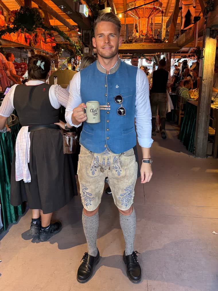 Ben in Lederhose und blauer Weste mit Krug im Wiesnzelt